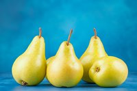 Fresh yellow pears arranged in row on vibrant blue background. Clean minimal food composition with ripe organic fruit for healthy eating concept.