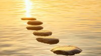 Stepping stones across calm golden water at sunset create path to bright sun reflection, representing spiritual journey and mindful meditation practice.