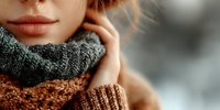 Young woman wearing cozy knitted scarf and sweater in warm autumn colors, soft natural lighting creates intimate winter fashion portrait for lifestyle content.