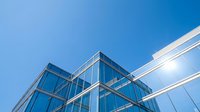 Modern glass and steel office building with geometric architecture against clear blue sky, suitable for corporate, business, and real estate design projects.