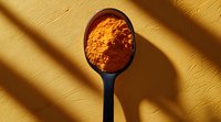 Vibrant orange turmeric powder in black measuring spoon casting dramatic diagonal shadows on textured yellow surface, minimalist food photography composition.