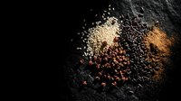Assorted grains, seeds and spices scattered on dark slate surface creating rustic culinary composition for cooking and healthy nutrition concepts.