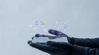 A hand wearing black gloves holds a digital network visualization with connected nodes and lines floating above the palm against a light gray background.
