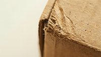 Damaged brown cardboard box corner with torn edges and frayed fibers showing wear and tear from shipping or handling.