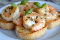 Succulent garlic shrimp appetizers served on toasted baguette rounds with fresh herbs and basil garnish, close up view of gourmet seafood bruschetta on white plate.