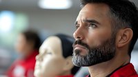 Middle-aged Caucasian man with beard in red shirt looking thoughtfully to side in modern office environment with blurred colleagues in background.