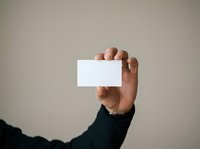 Middle-aged male hand holding blank white business card or paper against neutral background for corporate branding and marketing purposes.