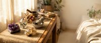 Cozy bedroom altar with crystals, candles, sage bundles and spiritual healing tools on wooden table creating peaceful meditation space for wellness rituals.