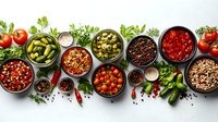 Fresh Mediterranean ingredients in black bowls on light background, including olives, tomatoes, peppers, herbs and spices. Food border composition with copy space.