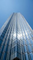 Modern glass skyscraper with reflective facade reaching toward blue sky, contemporary urban architecture for business and corporate design projects.