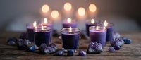 Purple candles burning in glass holders surrounded by amethyst crystals and gemstones on rustic wooden surface with warm bokeh lights background for spa relaxation.