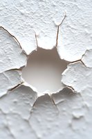Cracked hole in white textured wall surface showing rough edges and depth. Dramatic lighting creates shadow effect, highlighting structural damage pattern.