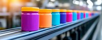 Colorful paint cans arranged in row on industrial conveyor belt with selective focus. Manufacturing facility production line showing vibrant packaging containers.