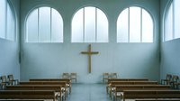 Serene church interior with wooden pews, arched windows, and golden cross on pale blue wall, suitable for religious and spiritual design projects.