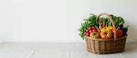 Fresh organic vegetables and fruits in wicker basket on white marble counter, healthy eating concept for kitchen design and nutrition lifestyle.