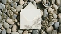 Elegant white envelope surrounded by smooth river stones and dried botanicals creating natural spa-like composition for wellness branding and stationery design.