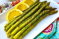 Fresh grilled asparagus spears garnished with orange slices on white plate, served on colorful floral pattern cloth, close up view of healthy vegetarian dish.
