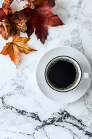 Cup of black coffee on marble surface with autumn maple leaves in red and orange tones creating seasonal composition for social media and blogs.