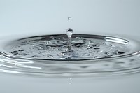 Water droplet creating ripples on clear liquid surface with splash crown formation in macro photography for wellness and purity concepts.