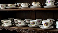 Collection of vintage floral porcelain teacups and saucers displayed on wooden shelves, antique china set with delicate flower patterns for tea service.