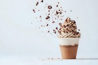 Chocolate milkshake topped with whipped cream and flying chocolate pieces against white background. Dynamic food photography with splash effect.