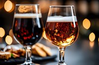 Two glasses of wine, one red and one white, with sparkling bubbles and golden bokeh lights in background, accompanied by appetizers and snacks on plate, suitable for beverage, dining, celebration and hospitality design projects.