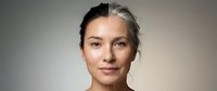 Middle-aged Caucasian woman with natural gray hair and glowing skin showcasing aging gracefully and self-acceptance in neutral studio portrait.