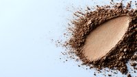Loose mineral makeup powder in bronze shade scattered on white background, creating natural texture for cosmetic product photography.