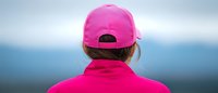 Young woman in bright pink sportswear and baseball cap looking at horizon, back view panoramic shot showing active lifestyle and contemplation outdoors.