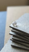 Single sparkling diamond gemstone resting on stack of gray textured material samples showcasing luxury jewelry and interior design elements.