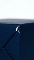Torn blue fabric with white rip showing damage and wear on textile material surface creating abstract pattern with dramatic lighting and shadows.