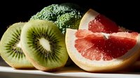 Sliced kiwi fruit and grapefruit halves with fresh broccoli florets arranged on dark background for food photography and healthy eating concepts.