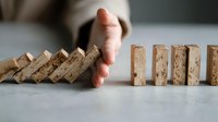 Hand stopping falling wooden dominoes, symbolizing crisis management and risk prevention in business strategy and problem-solving concepts.