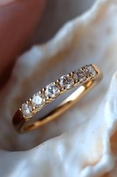 Elegant gold wedding band with five brilliant diamonds in classic setting against soft white background, luxury jewelry photography for bridal collections.