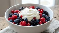 Fresh mixed berries with cream in white bowl on rustic wooden table. Healthy breakfast dessert with raspberries blueberries blackberries and whipped cream.