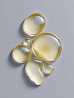 Golden oil drops or bubbles on gray background, macro photography showing transparent liquid texture with light reflections and sparkles. Suitable for cosmetic advertising.
