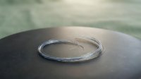 Silver bangle bracelet with brushed finish resting on dark sphere surface, minimalist jewelry design for fashion and accessories stock use.