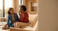 Happy African American mother and teenage daughter laughing together on living room sofa during warm conversation at home.