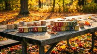 Wooden alphabet blocks spelling AUTUMN and NATURE on rustic table with colorful fall leaves scattered around in golden forest setting.