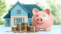 Pink ceramic piggy bank with stacked gold coins in front of blue house, representing home savings, mortgage and real estate investment concept.