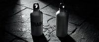Two black spray paint cans on textured concrete surface with dramatic lighting and shadows, suitable for urban art, graffiti, street culture, and design projects.