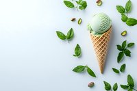 Pistachio ice cream scoop in waffle cone surrounded by fresh mint leaves and nuts on light background. Refreshing summer dessert composition.