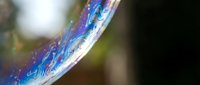 Iridescent soap bubble surface with rainbow colors and reflective patterns floating in air with blurred natural background for creative projects.