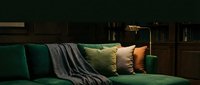 Emerald green velvet sofa with decorative pillows and throw blanket in modern living room interior design setting.