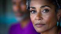 Close up portrait of mature African American woman with natural makeup and turquoise earrings looking thoughtfully to side against blurred background.