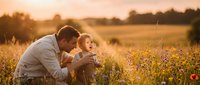 Father and toddler son exploring wildflower meadow during golden hour sunset, bonding moment in nature with warm sunlight creating peaceful family scene.