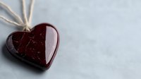 Red glass heart pendant on string against light gray background, romantic jewelry piece with glossy surface and delicate details for Valentine's Day designs.