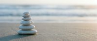 Zen stone stack balanced on sandy beach with soft ocean waves in background creating peaceful meditation and mindfulness concept for wellness and relaxation.