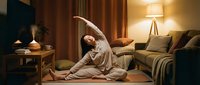 Young woman practicing yoga side bend stretch in cozy bedroom with warm lighting and modern decor for wellness and relaxation routine.