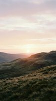 Golden sunrise illuminates rolling hills and moorland valleys with soft warm light, creating serene landscape scenery for travel, nature, and editorial design projects.
